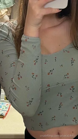 Woman in floral long-sleeve crop top, holding phone, indoor setting.