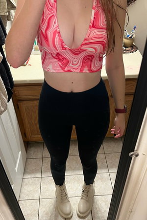 Woman in pink crop top and black leggings in bathroom.