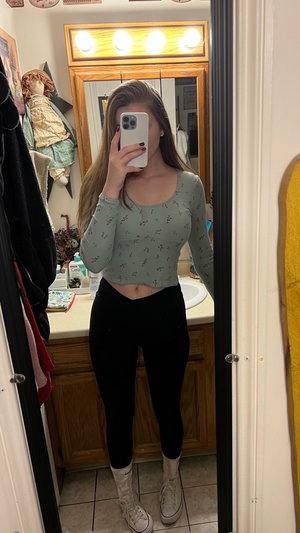 Woman taking mirror selfie in bathroom wearing crop top and leggings.