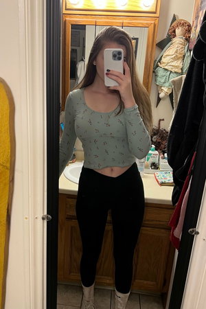 Woman taking mirror selfie in bathroom wearing crop top and leggings.