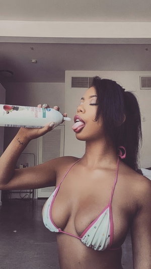 Woman in pink-trimmed bikini top drinking from a bottle indoors.