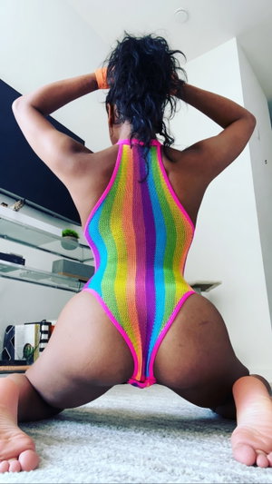 Woman in rainbow mesh bodysuit posing on carpet indoors, back view.