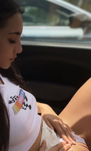 Woman in white crop top and lace underwear, sitting outdoors near a car.