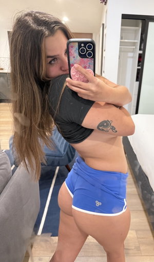 Woman taking mirror selfie in blue shorts indoors.