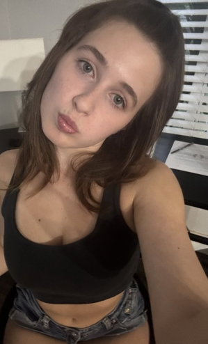 Brunette woman in black crop top and denim shorts indoors.