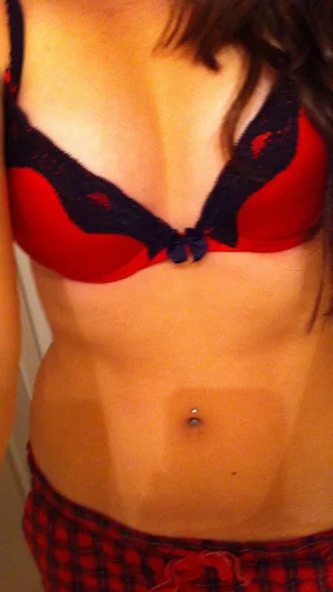 Woman in red and black lace bra and plaid bottoms, showing midriff with belly button piercing.