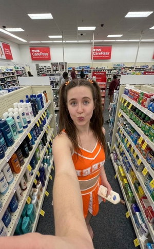 Woman with pigtails in orange cheerleader outfit in store aisle.