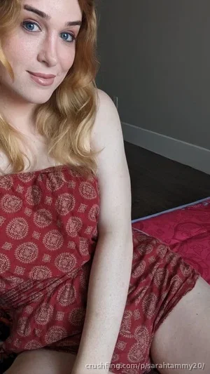 Woman with blonde hair in red patterned dress sitting indoors.