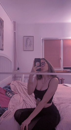 Brunette woman with glasses in black crop top taking bedroom selfie.