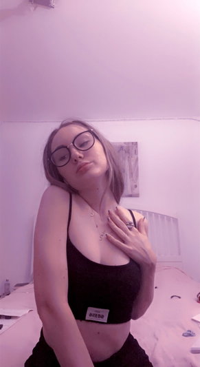 Blonde woman with glasses in black crop top posing in bedroom.