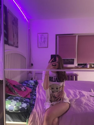 Woman in t-shirt taking mirror selfie on bed in purple bedroom.