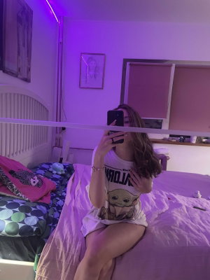 Woman in t-shirt taking selfie on bed under purple lights.