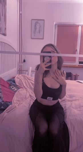 Woman taking selfie in bedroom wearing black crop top and skirt.