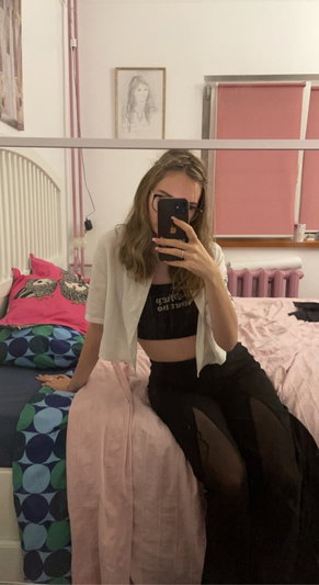 Woman with glasses taking selfie in bedroom wearing crop top.