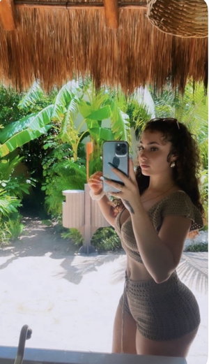 Woman in crochet outfit taking selfie in tropical setting.