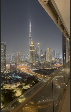Night cityscape view from balcony, featuring illuminated skyscrapers and urban lights.