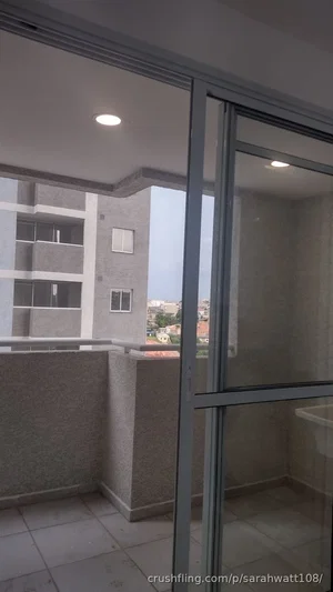Balcony view from inside a building with glass door, showing adjacent apartment and cityscape.