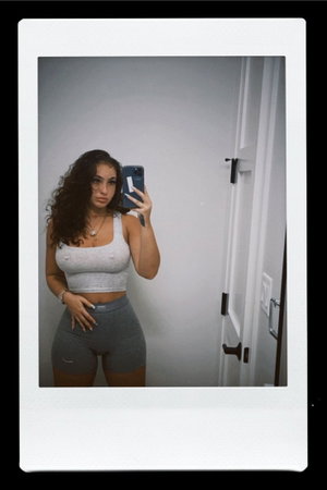 Curvy woman in gray tank and shorts, mirror selfie indoors.