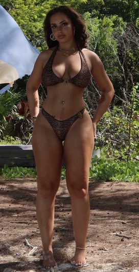 Woman in leopard print bikini standing outdoors in a wooded area.