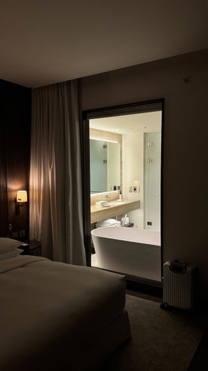 Hotel room with bed, bathtub, and bathroom visible through glass door.
