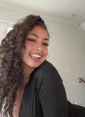 Woman with curly hair in black top smiling indoors.