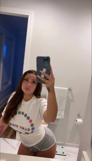 Curvy woman in white t-shirt and gray shorts in bathroom mirror selfie.