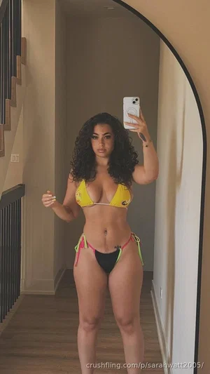 Woman in yellow and black bikini taking mirror selfie in indoor hallway.