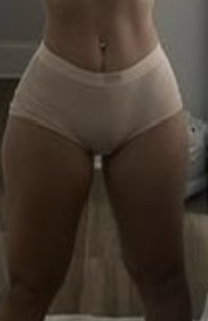 Woman in beige underwear standing indoors, showing midriff and legs.