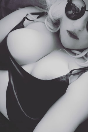 Curvy blonde woman in black top and sunglasses reclining indoors.