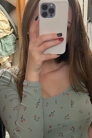 Woman with long brown hair in floral top taking mirror selfie indoors.