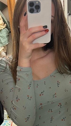 Woman with long brown hair in floral long-sleeve top taking mirror selfie indoors.