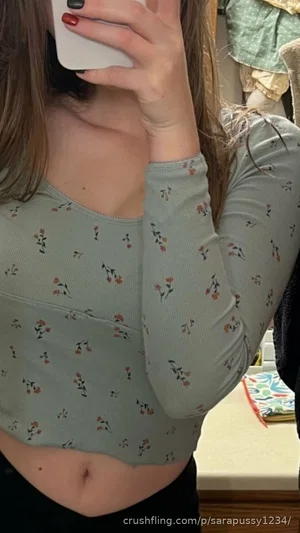 Woman in floral long-sleeve crop top, holding phone, indoor setting.