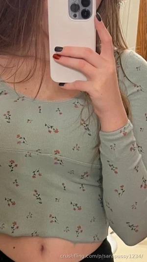 Woman in floral long-sleeve crop top taking mirror selfie, showing midriff.