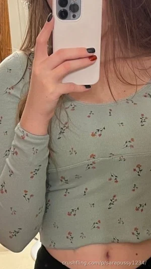 Woman in floral long-sleeve crop top taking mirror selfie, showing midriff.