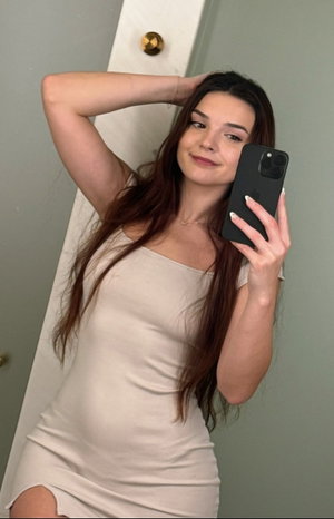 Curvy brunette in beige mini dress takes indoor selfie.