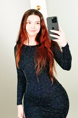 Woman with red hair in black sparkly dress, mirror selfie.