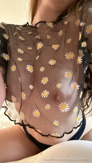 Woman in sheer floral top and black underwear, sitting indoors.