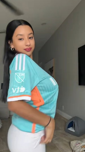 Woman with long dark hair wearing turquoise jersey indoors.