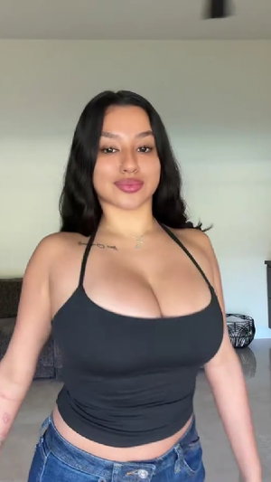 Curvy woman with dark hair in black top and jeans indoors.