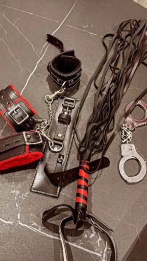 BDSM gear including cuffs, whip, and restraints on a marble surface.