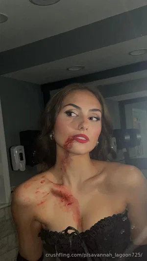 Woman in black lace top with red makeup on face and chest, indoors.