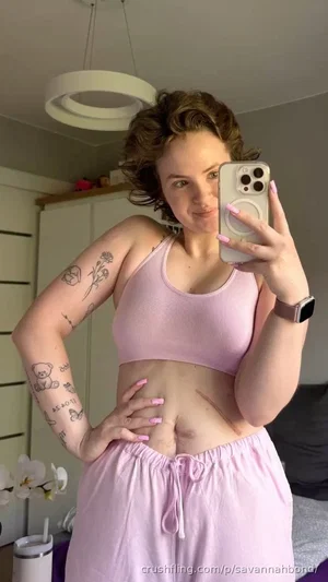 Woman with curly hair and tattoos wears pink sports bra and matching pants, taking mirror selfie in