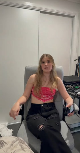 Blonde woman in pink top and black jeans sitting in chair.
