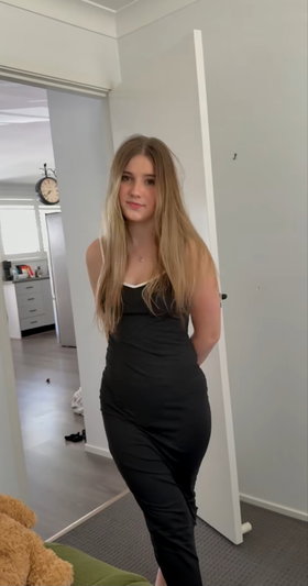 Blonde woman in black dress standing indoors near doorway.