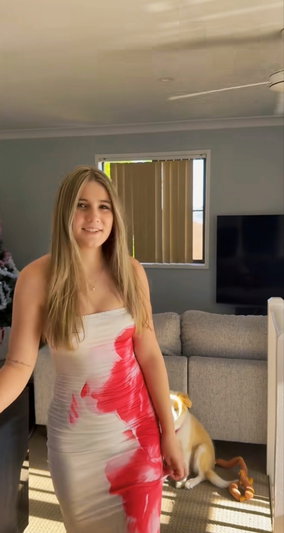 Blonde woman in patterned dress standing indoors with dog.