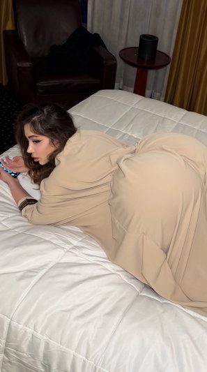Woman in beige dress lying on bed using phone.