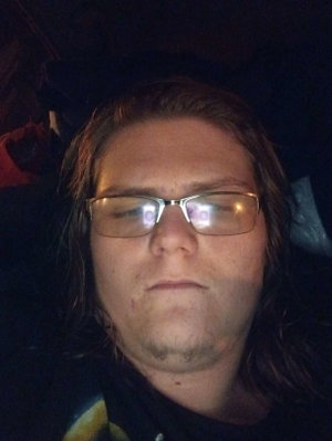Person with long hair and glasses, wearing dark clothing, in dim lighting.