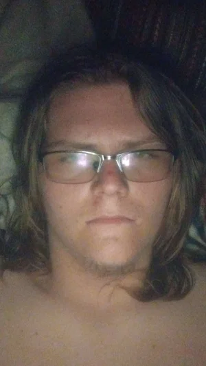 Shirtless person with long hair and glasses lying down indoors.