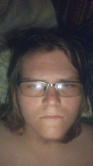 Person with glasses and shoulder-length hair, bare chest, lying down indoors.