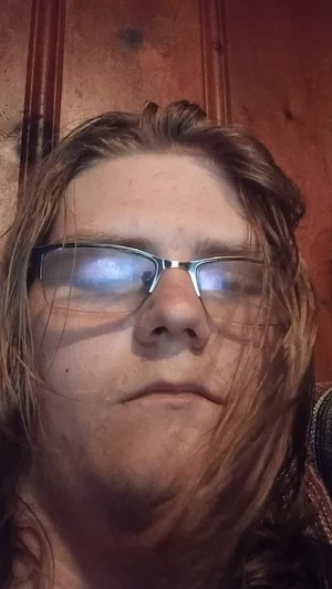 Person with long hair and glasses, indoor setting, close-up face shot.
